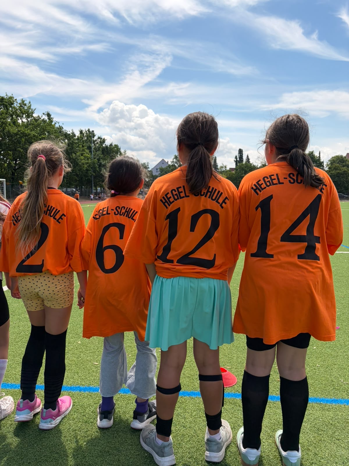 Kinder einer Fußballmannschaft in orangefarbenen Trikots am Spielfeldrand