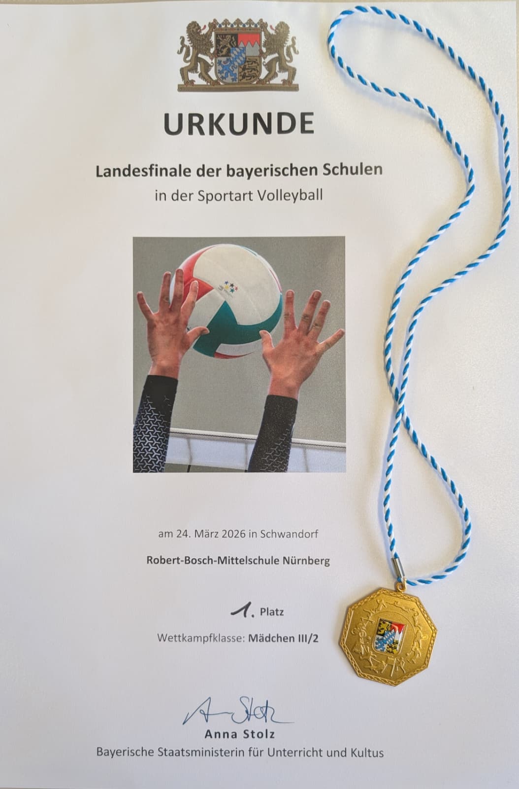 Urkunde und Goldmedaille für den ersten Platz der Robert-Bosch-Mittelschule beim Landesfinale Volleyball 2026